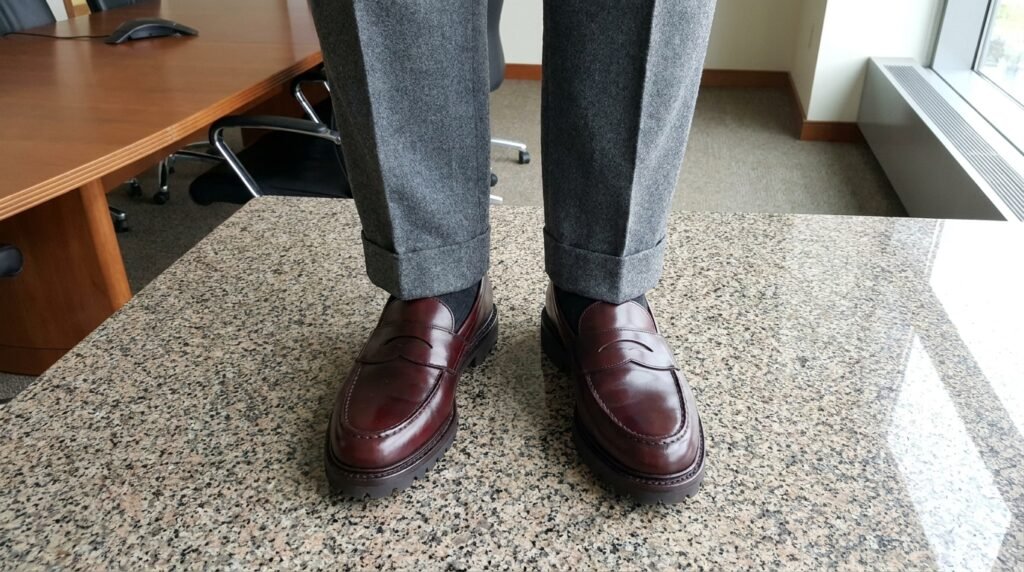 Polished burgundy leather penny loafers worn with grey pleated trousers for an interview.