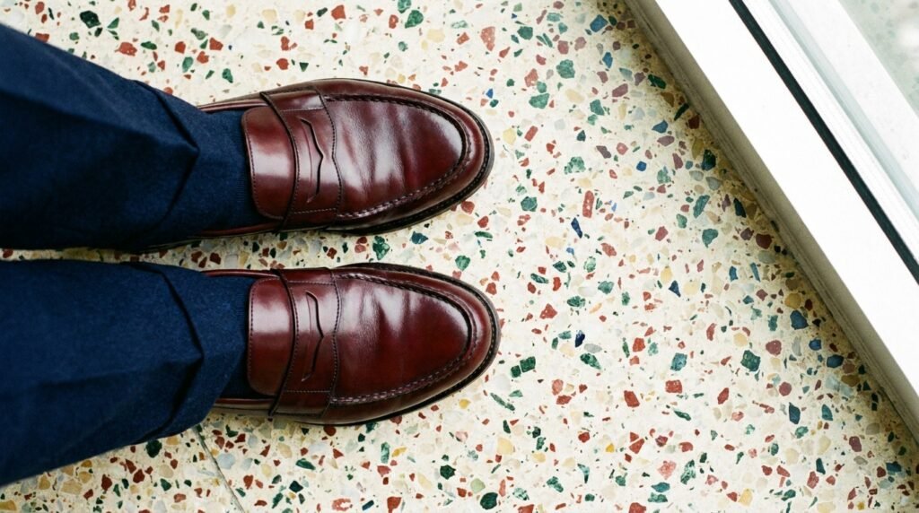 Polished burgundy leather penny loafers paired with navy pleated trousers.