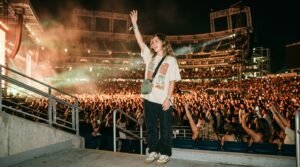 A concertgoer wearing retro sneakers cheering in a crowd at an illuminated stadium night concert.