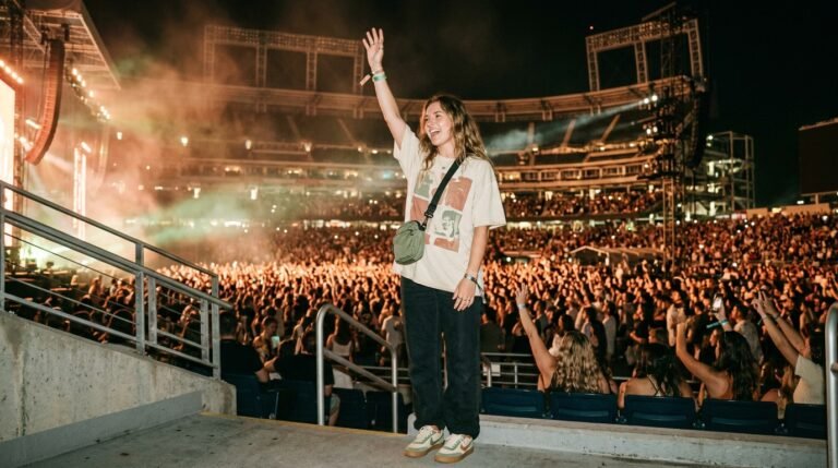 A concertgoer wearing retro sneakers cheering in a crowd at an illuminated stadium night concert.